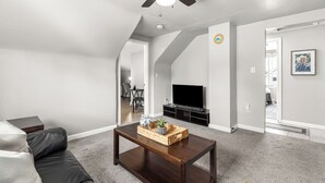 Una sala de estar con una mesa de centro marrón oscuro, un sofá de cuero negro, un ventilador de techo y un televisor de pantalla plana.