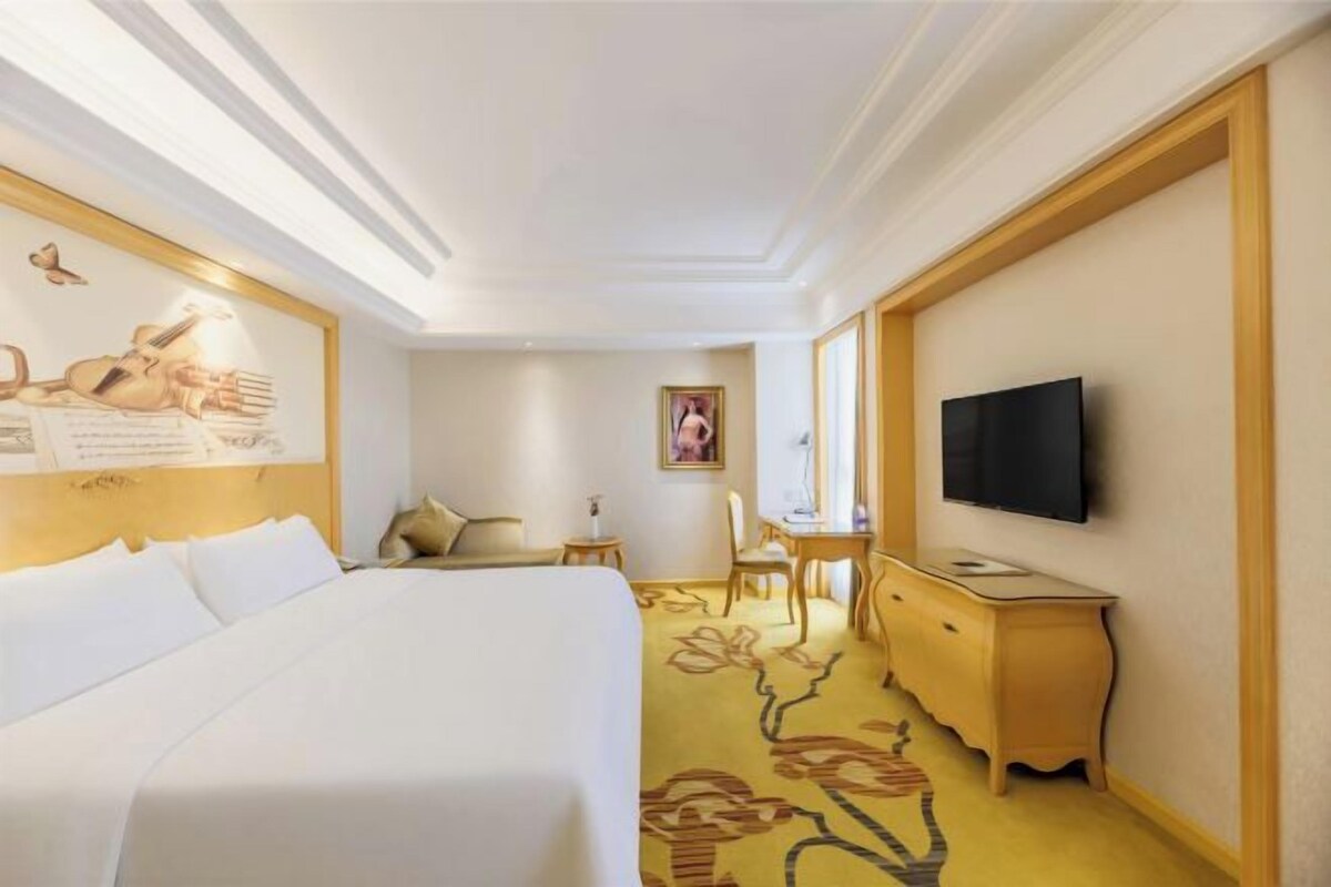 Una habitación de hotel con cama, escritorio, televisor y alfombra estampada.