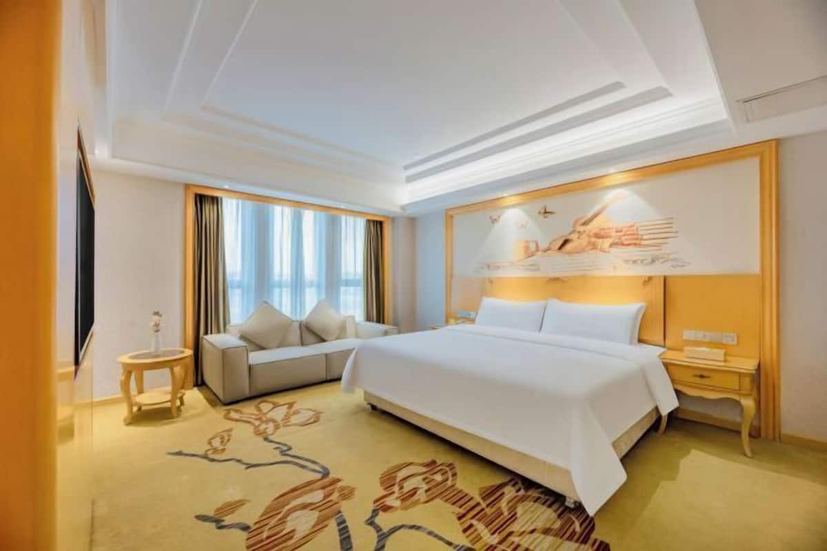 A hotel room with a large bed, a sofa, a small table, and a nightstand.