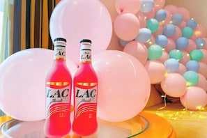 Two bottles of LAC champagne, pink and red, on a glass table with a yellow base, surrounded by pink and blue balloons. - Vienna International Hotel Nanning Wuyi Fude (Nanning)
