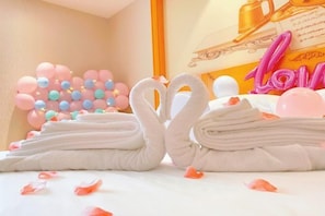 A neatly arranged stack of towels with a decorative swan shape made from towels, a wall with a 'Love' sign, and a balloon arrangement. - Vienna International Hotel Nanning Wuyi Fude (Nanning)