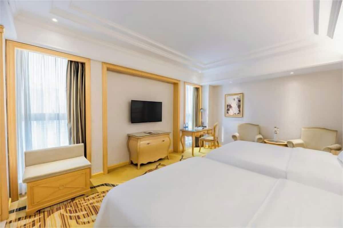 A hotel room with a large bed, a TV, a desk, and a chair.