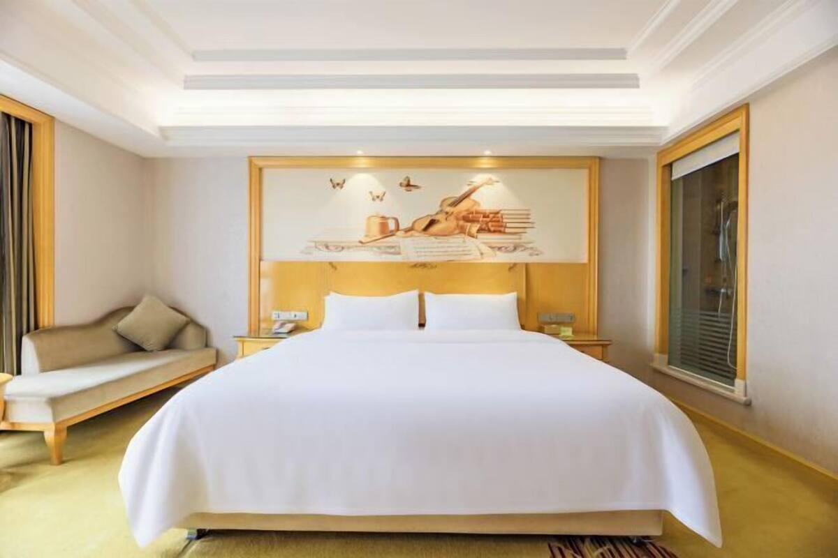 A hotel room with a large bed, a sofa, a nightstand, and a wall-mounted artwork.