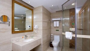 A modern bathroom with a large mirror, a sink, a toilet, and a glass-enclosed shower area. - Vienna International Hotel Nanning Wuyi Fude (Nanning)