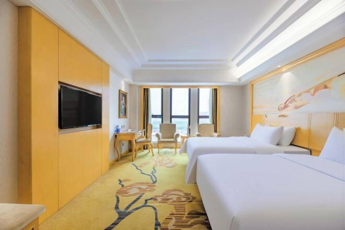 A hotel room with two beds, a TV, a desk, and a chair.