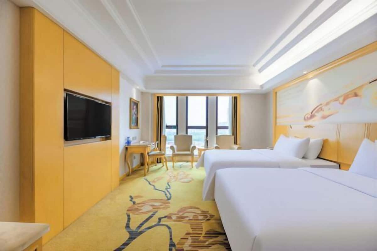A hotel room with two beds, a TV, a desk, and a chair.