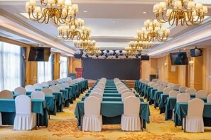 A conference room with rows of tables and chairs, chandeliers, and a stage. - Vienna International Hotel (Nanning Wuyi Fude) (Nanning)