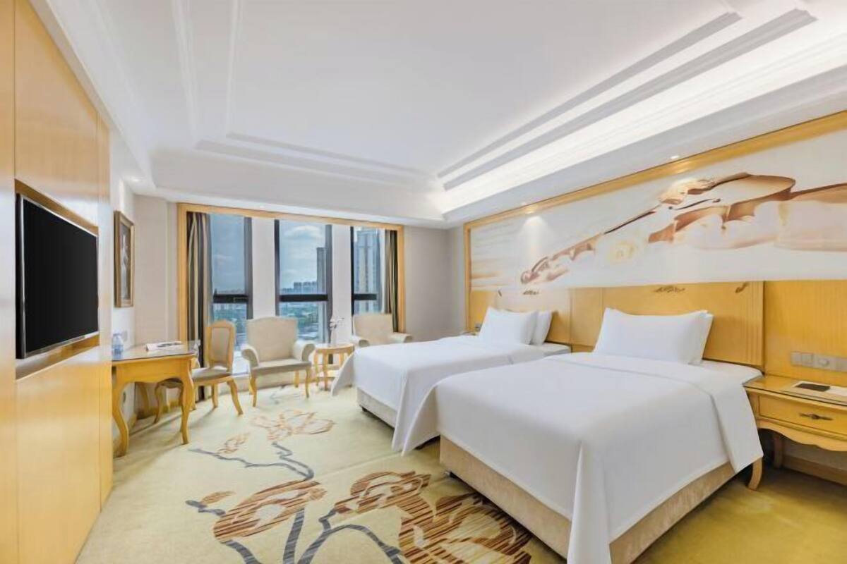 A hotel room with two beds, a TV, a desk, and a chair.