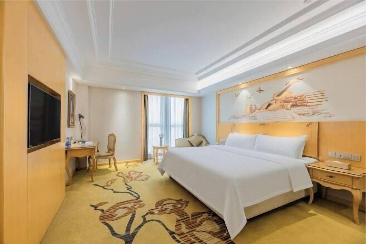 A hotel room with a bed, a desk, a chair, a TV, and a large window.