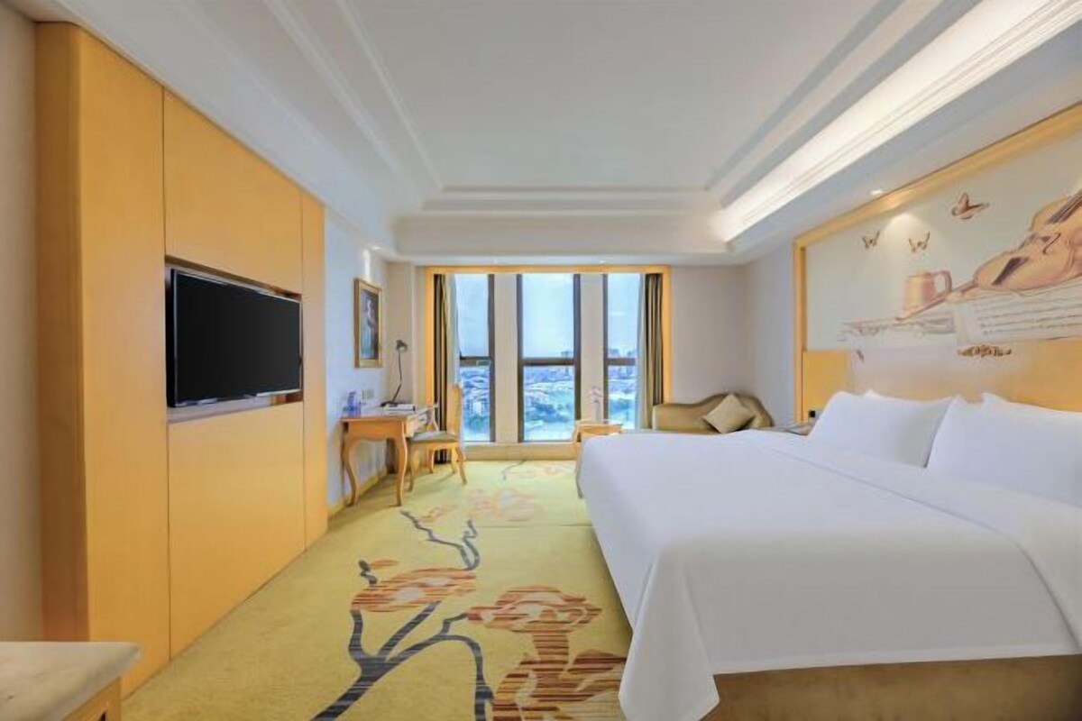Una habitación de hotel con una cama grande, televisión de pantalla plana, escritorio y ventana con vistas.