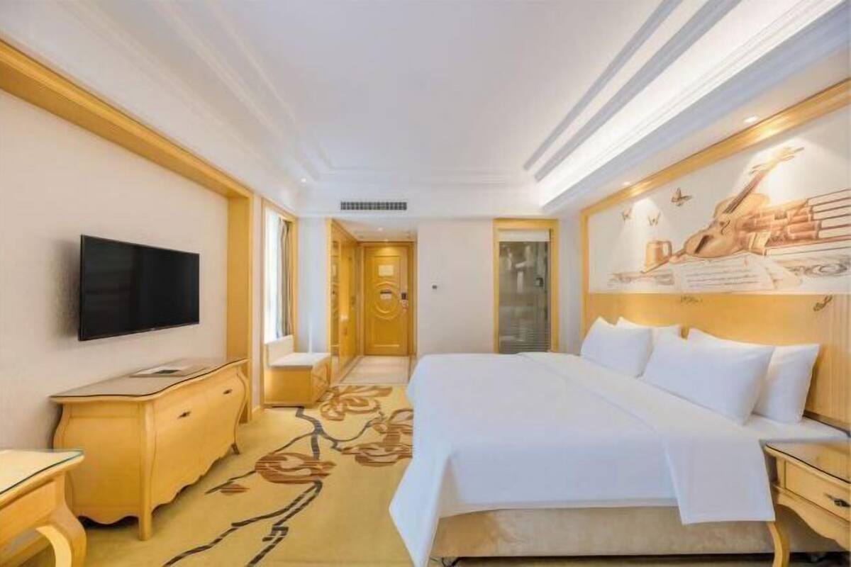 A hotel room with a large bed, a flat-screen TV, a wooden dresser, and a wall-mounted artwork.