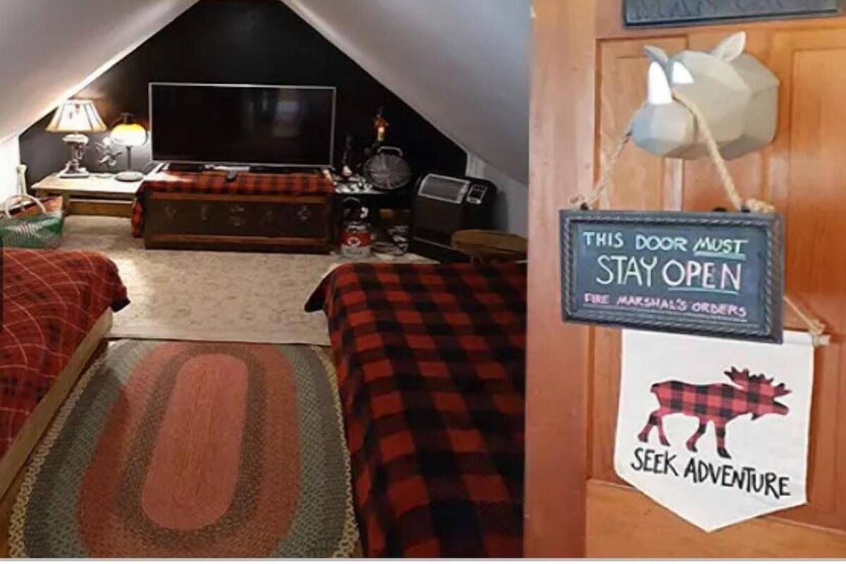 A cozy attic bedroom with a large TV, a fireplace, and a sign that reads "This door must stay open."