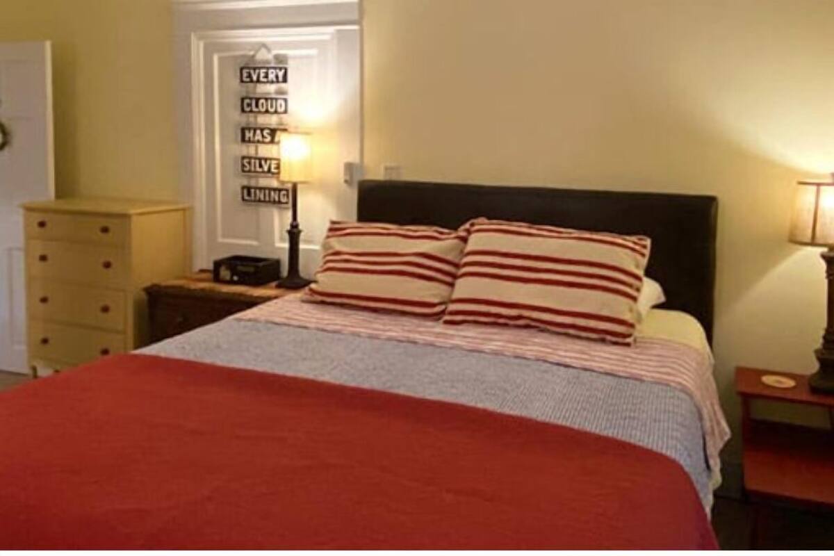A neatly made bed with striped pillows, a bedside lamp, and a wall sign.