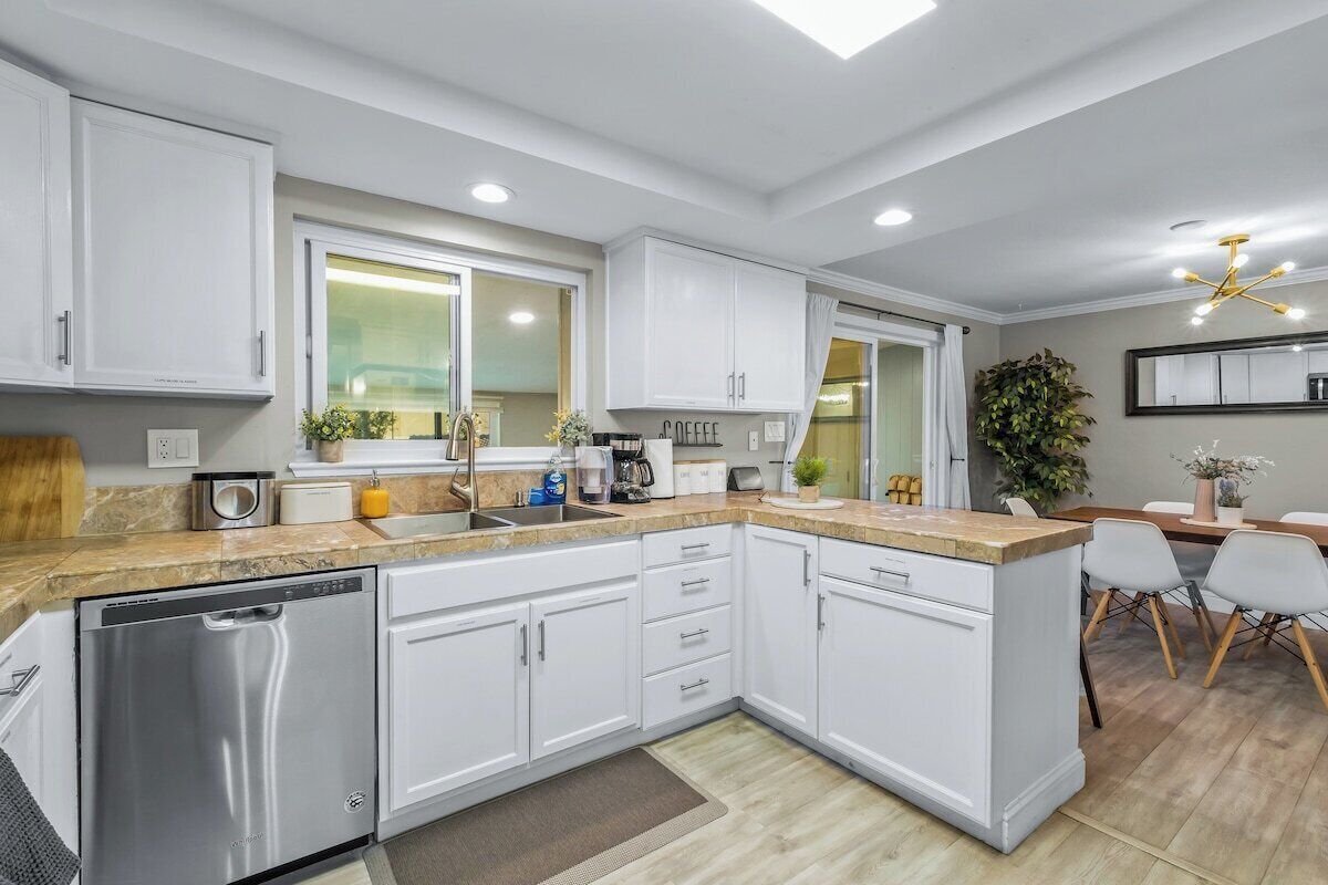 A modern kitchen with white cabinets, a dishwasher, and a countertop with various appliances.