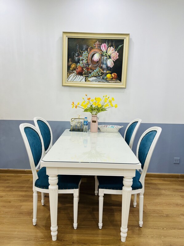 A dining table with four chairs, a painting above it, and a vase with yellow flowers on the table.