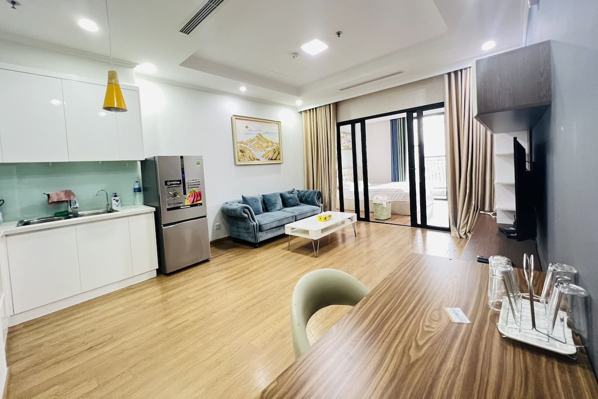 A modern hotel room with a kitchenette, a sofa, a dining table, and a TV.