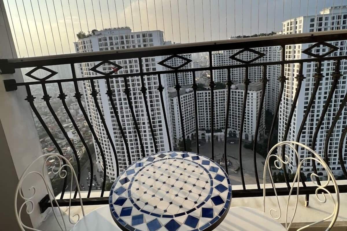 A balcony with a tiled table and two chairs, overlooking a cityscape with high-rise buildings.