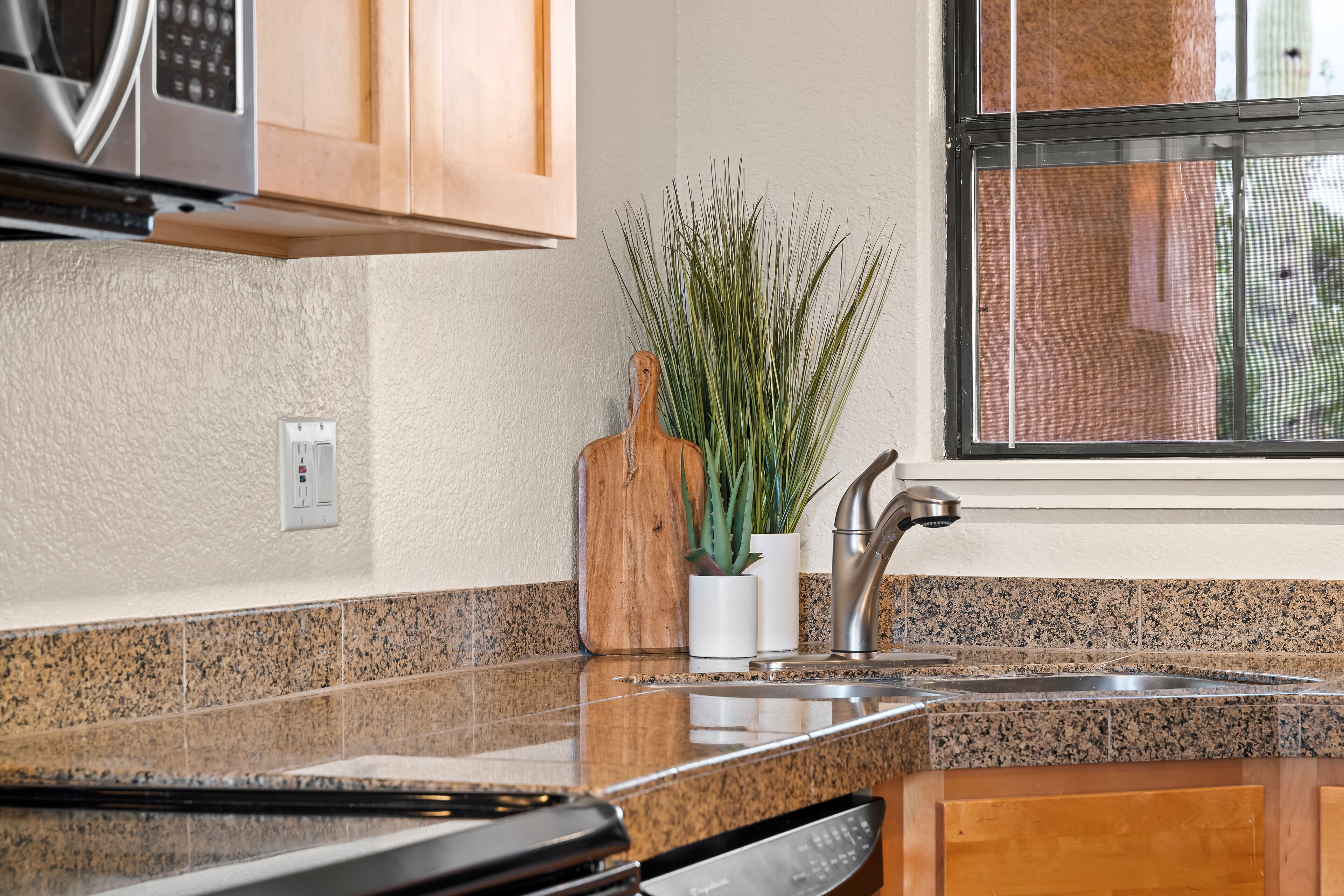 A kitchen with granite countertops, wooden cabinets, a stainless steel sink, and a window with a view of the outside.