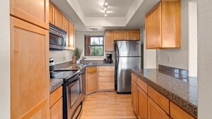 Una cocina moderna con armarios de madera, electrodomésticos de acero inoxidable, encimeras de granito y un ventanal que proporciona luz natural.