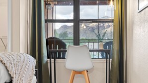 Una habitación con cama, una silla, una mesa y ventana con vistas a montañas.