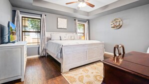 Une chambre à coucher comprenant un lit, un bureau, une chaise, un ventilateur de plafond et une fenêtre avec des rideaux.