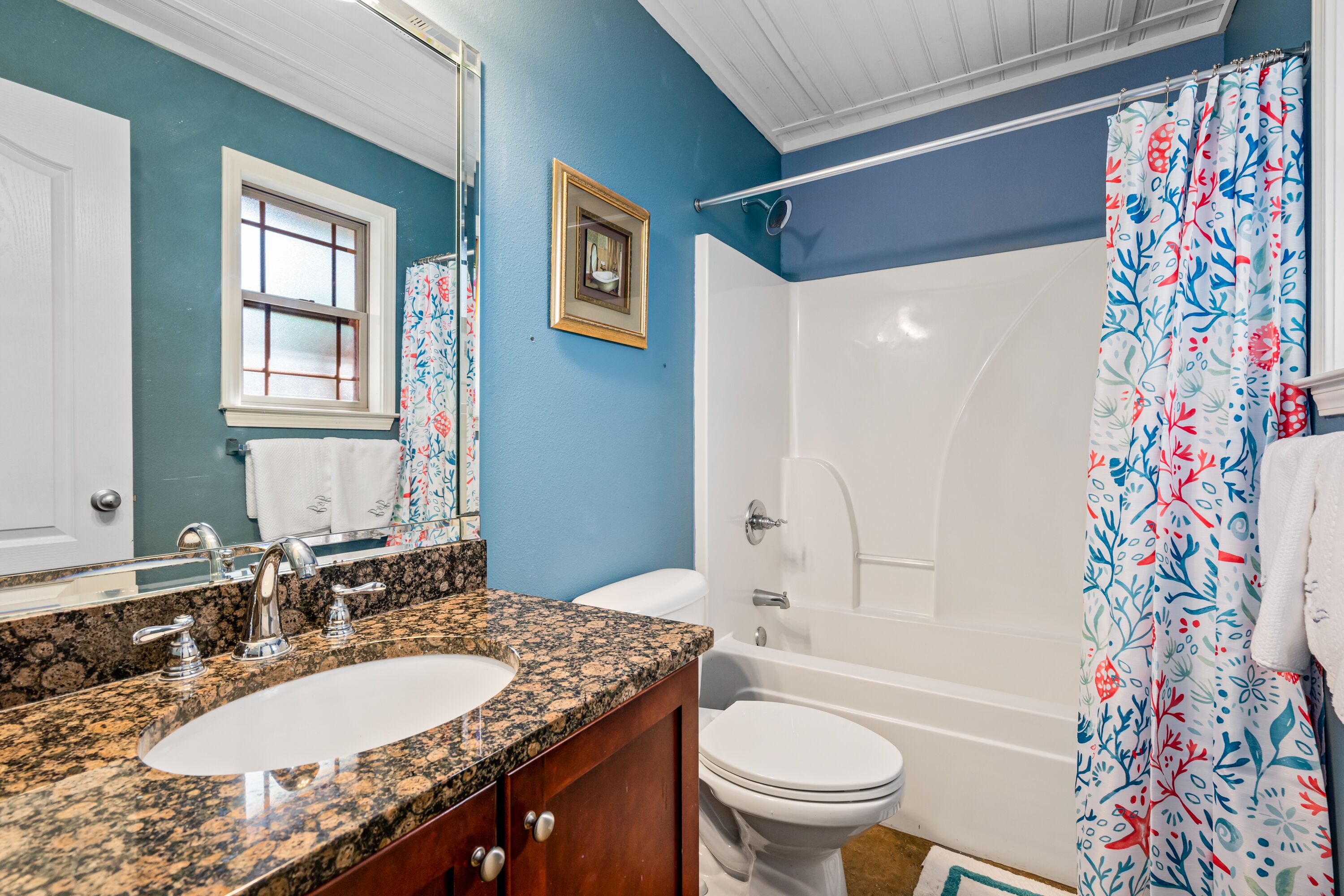 A bathroom with a granite countertop sink, a white toilet, and a bathtub.