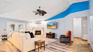 Un salon spacieux avec un canapé, une cheminée, un téléviseur et un ventilateur de plafond.