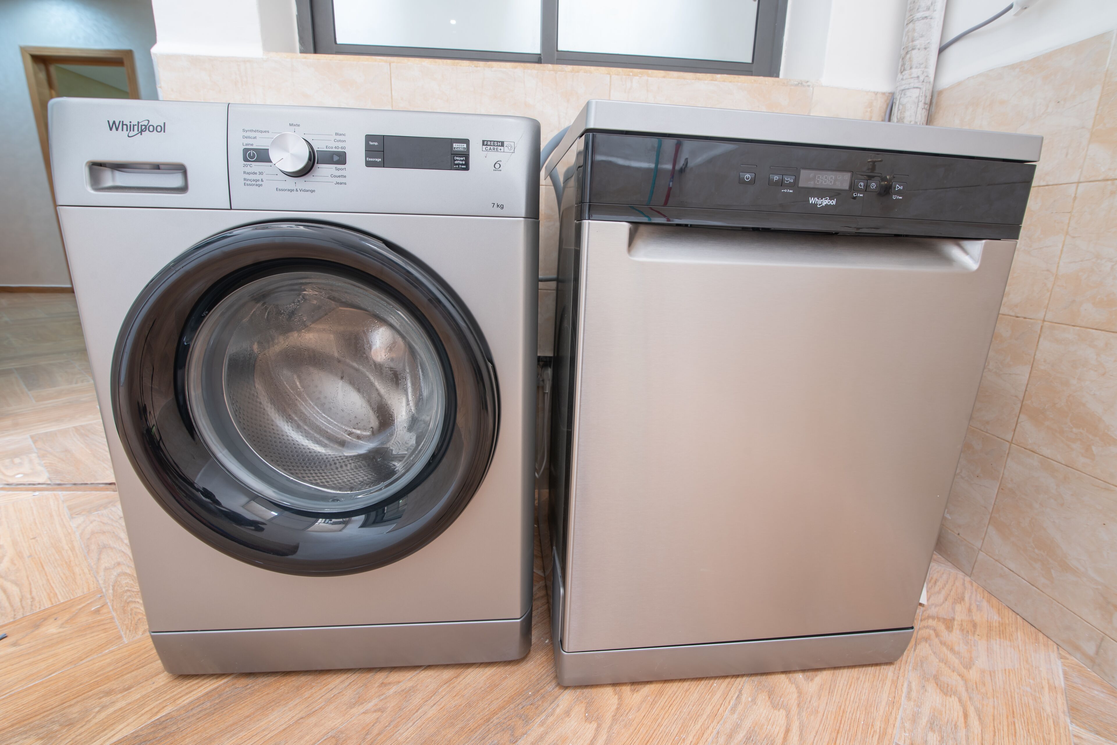 Un appareil combiné lave-linge et sèche-linge Whirlpool à chargement frontal, doté d’un panneau de commande, situé dans une pièce dont le sol est recouvert de parquet.