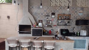 An outdoor kitchen with a built-in oven, bar stools, and a tiled backsplash. - Beautiful house on the best beach in Caraguatatuba. (Ubatuba)