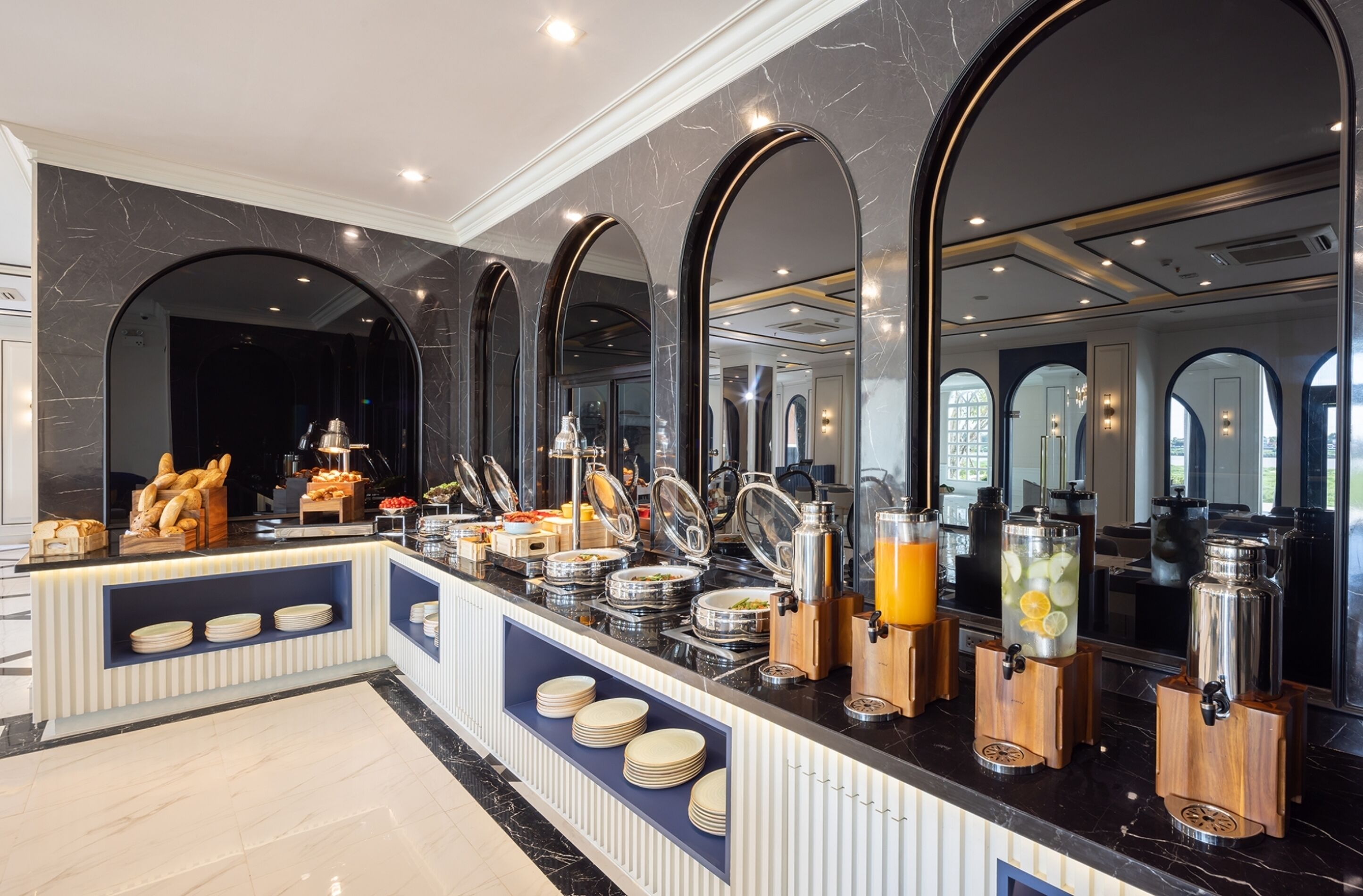 A breakfast buffet with various food items and beverages, a marble wall, and a large mirror.