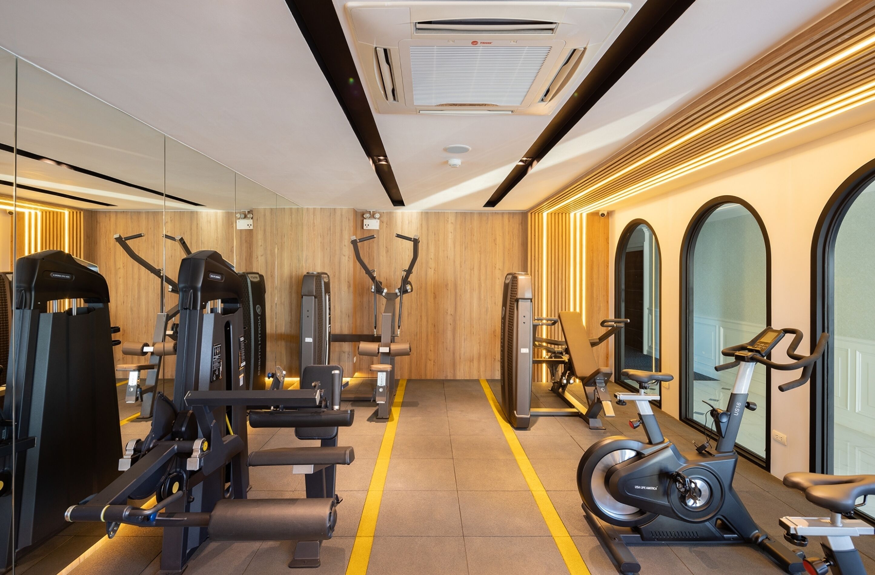 A gym with various exercise machines, a mirrored wall, and a wooden floor.