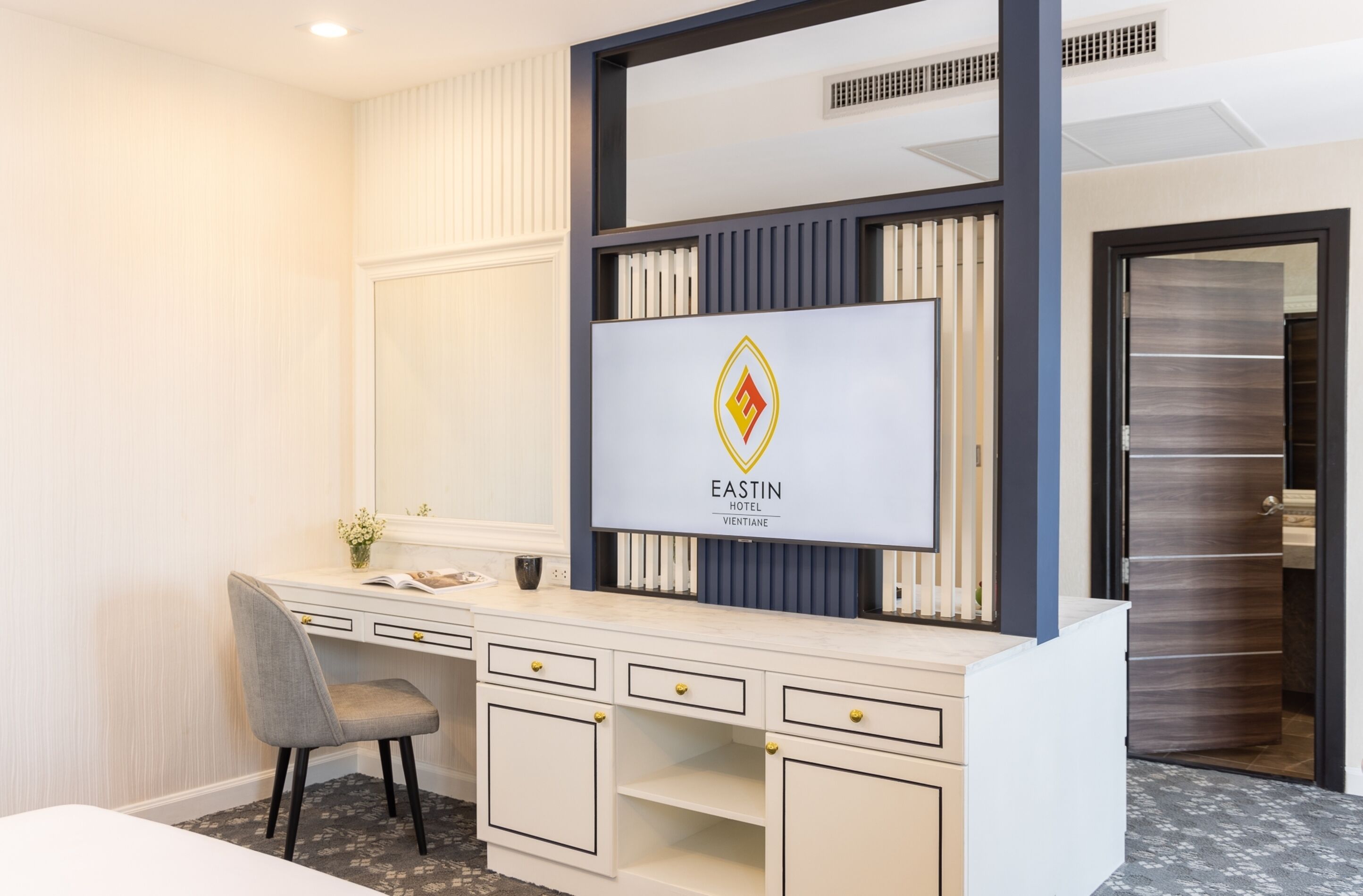 A hotel reception desk with a modern design, a large mirror, and a logo for Eastin Hotel.