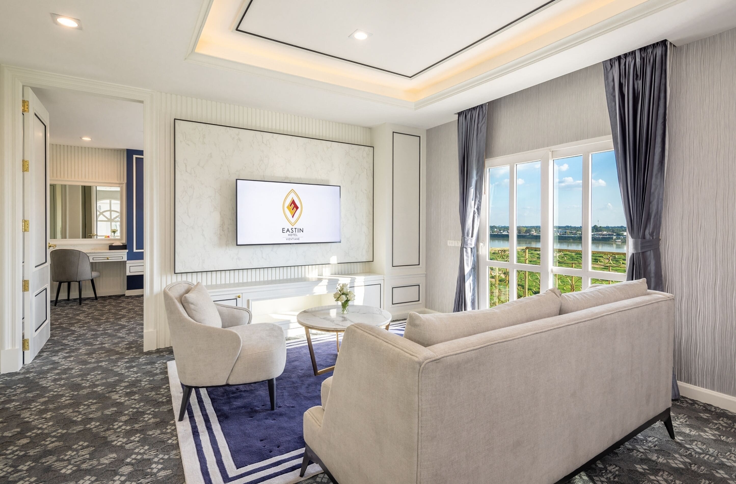 Une chambre d’hôtel avec une grande fenêtre, un canapé, une télévision et un bureau.