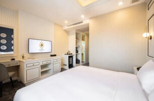 A hotel room with a large bed, a desk with a flat-screen TV, a wardrobe, and a walk-in closet.