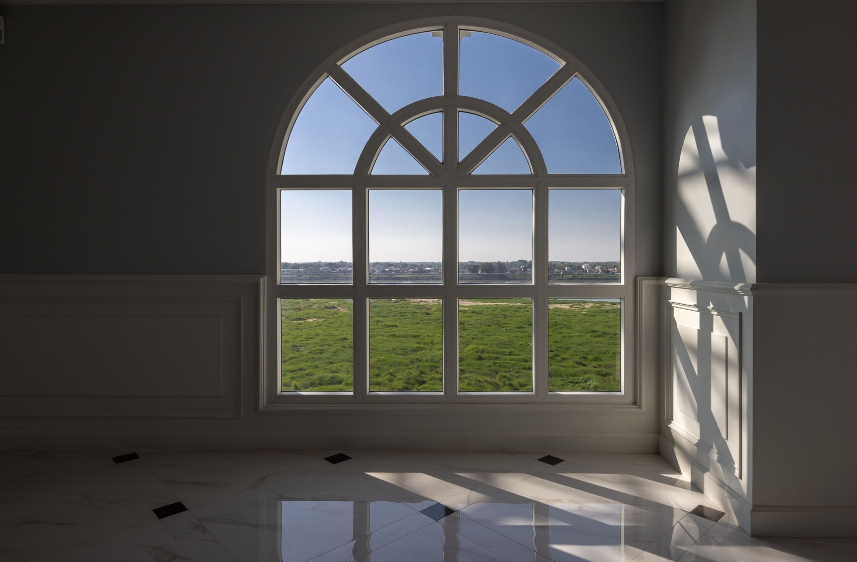 A room with a large arched window, a tiled floor, and a view of a green field.