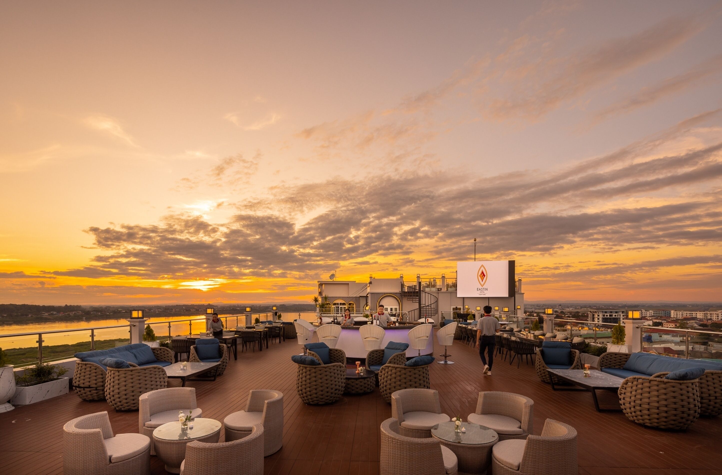 A rooftop terrace with outdoor seating and a view of the sunset over a body of water.