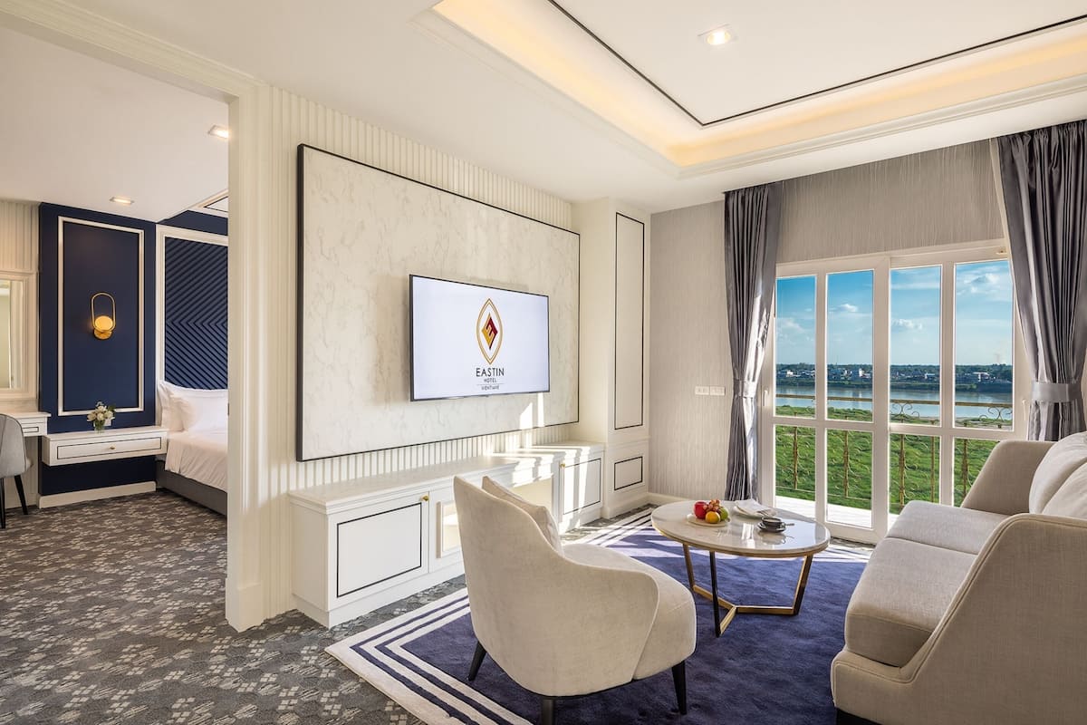 Une chambre d’hôtel équipée d’un lit, d’un bureau, d’un téléviseur fixé au mur, d’un canapé et d’une grande fenêtre donnant sur un beau paysage.