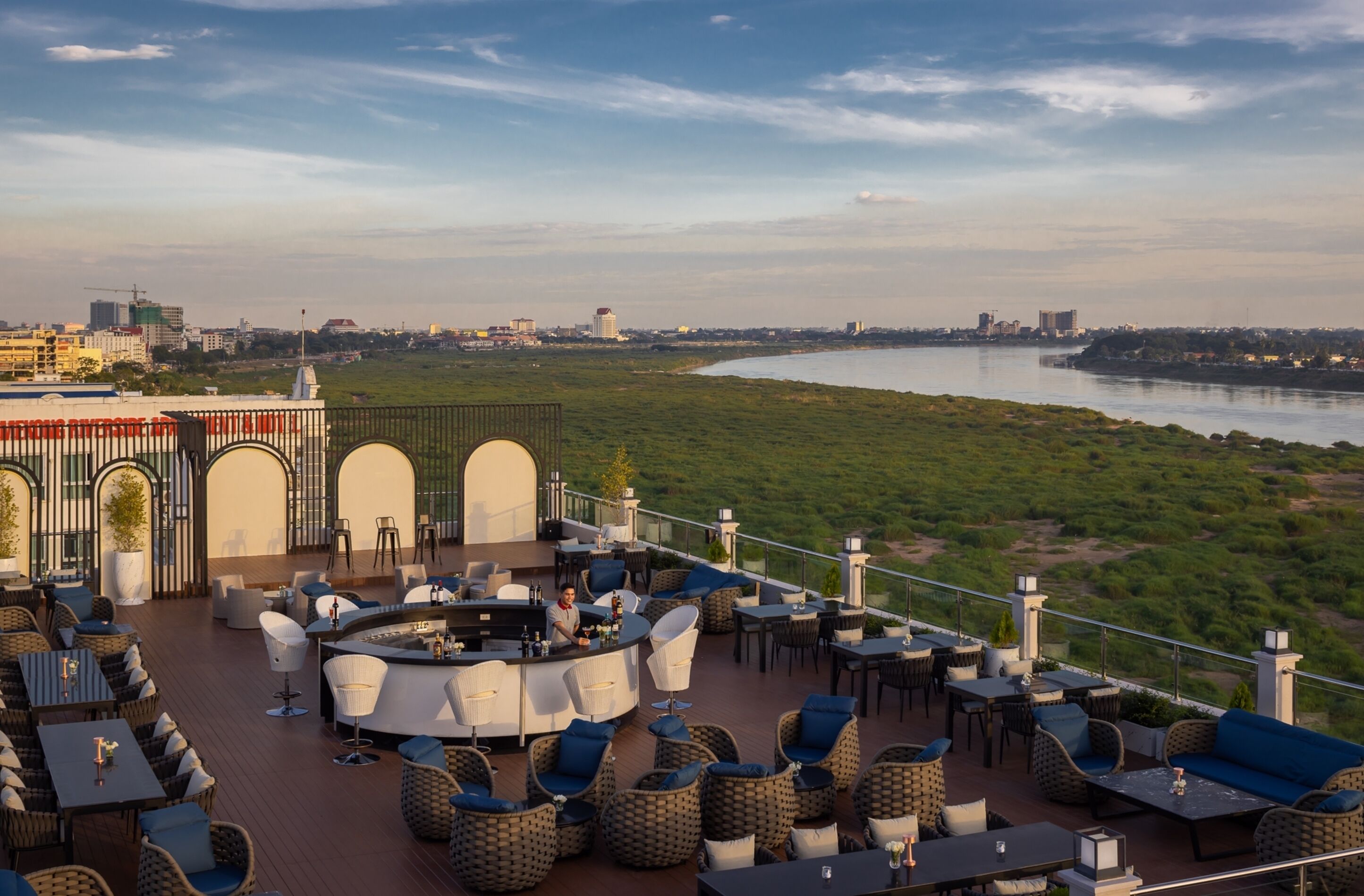 A rooftop bar with outdoor seating, overlooking a river and cityscape.