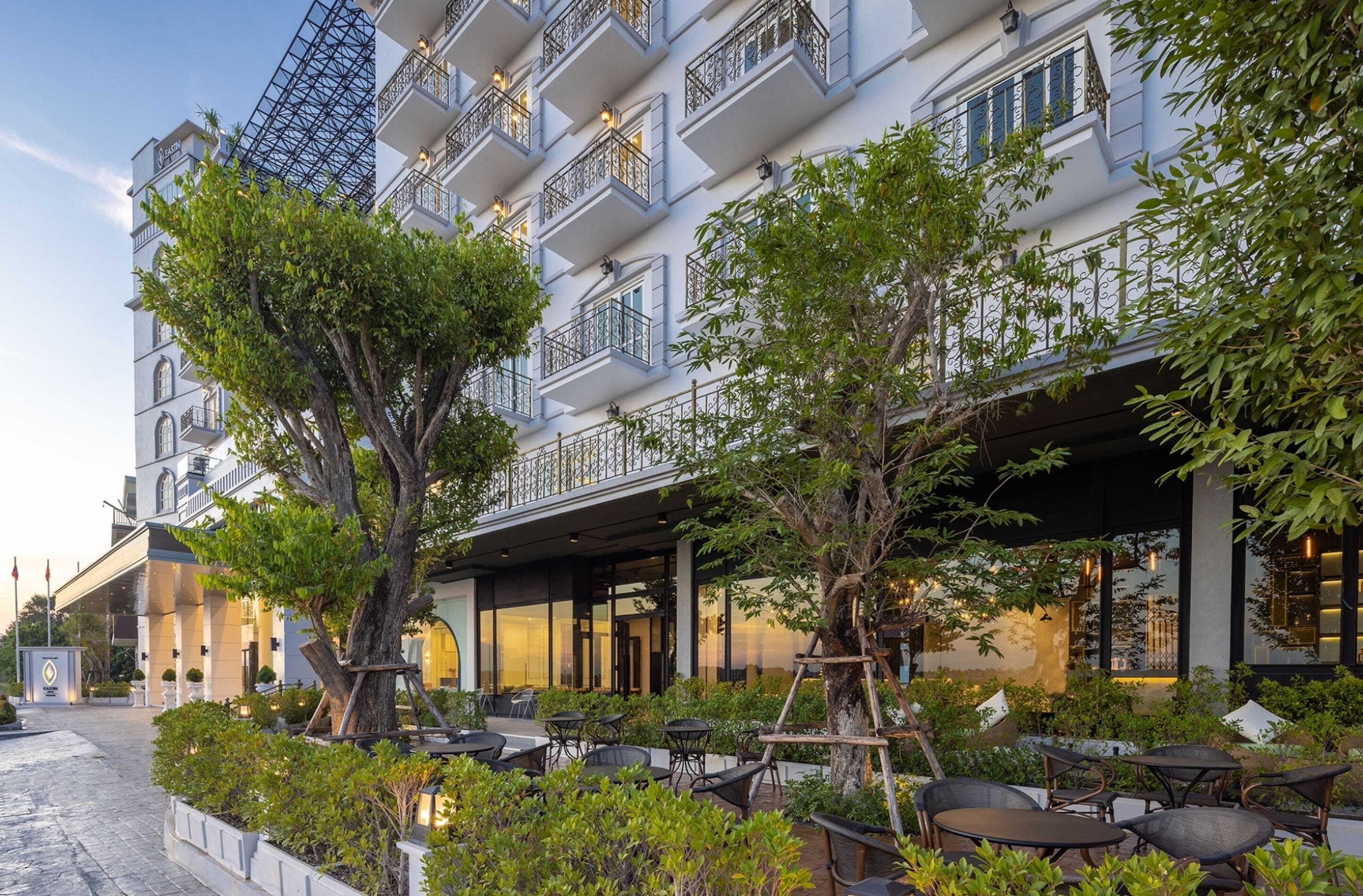 A hotel with outdoor seating, a covered area, and a large tree in the foreground.