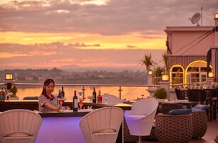 Eine Bar mit Korbstühlen und Blick auf den Sonnenuntergang über dem Wasser.