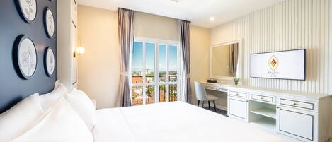 Habitación de hotel con una cama grande, un escritorio con televisor y un balcón con vistas.