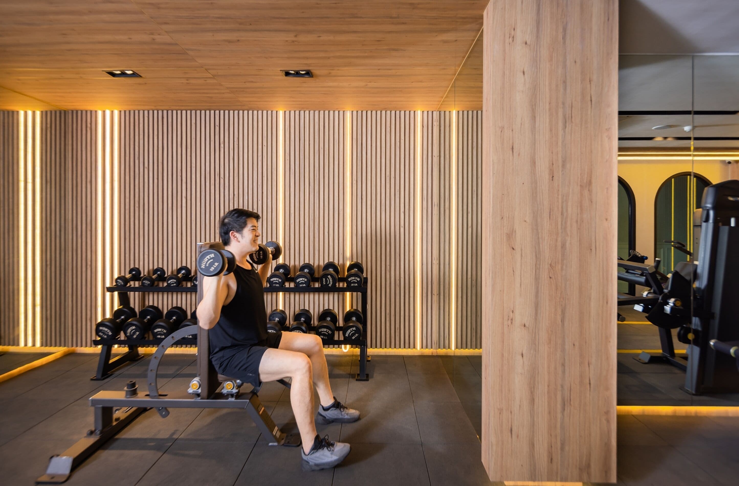 A gym with a wooden wall, exercise equipment, and dumbbells.