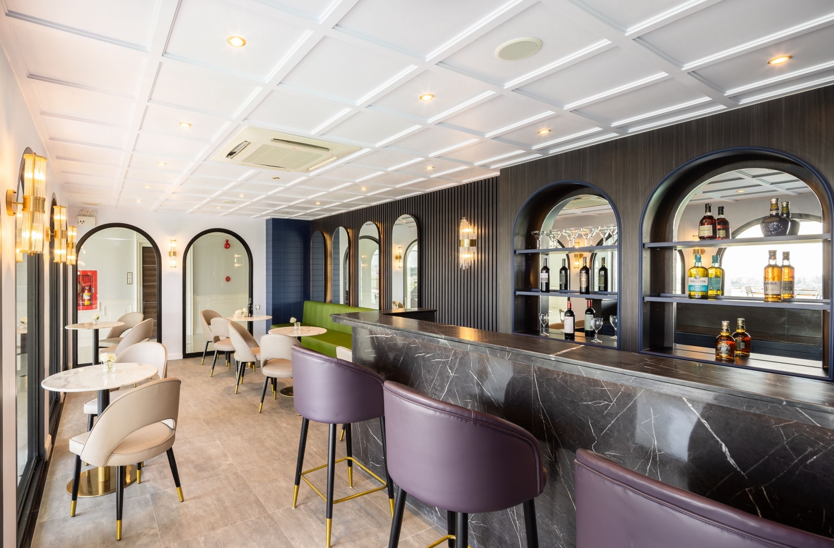 Eine moderne Bar mit Marmorplatten, violetten Barhocker und einer Auswahl an Flaschen in Regalen.