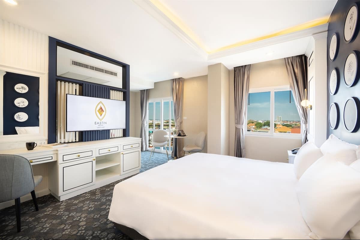 Une chambre d’hôtel avec un grand lit, un bureau doté d’un téléviseur à écran plat, une chaise et une vue sur la ville par la fenêtre.