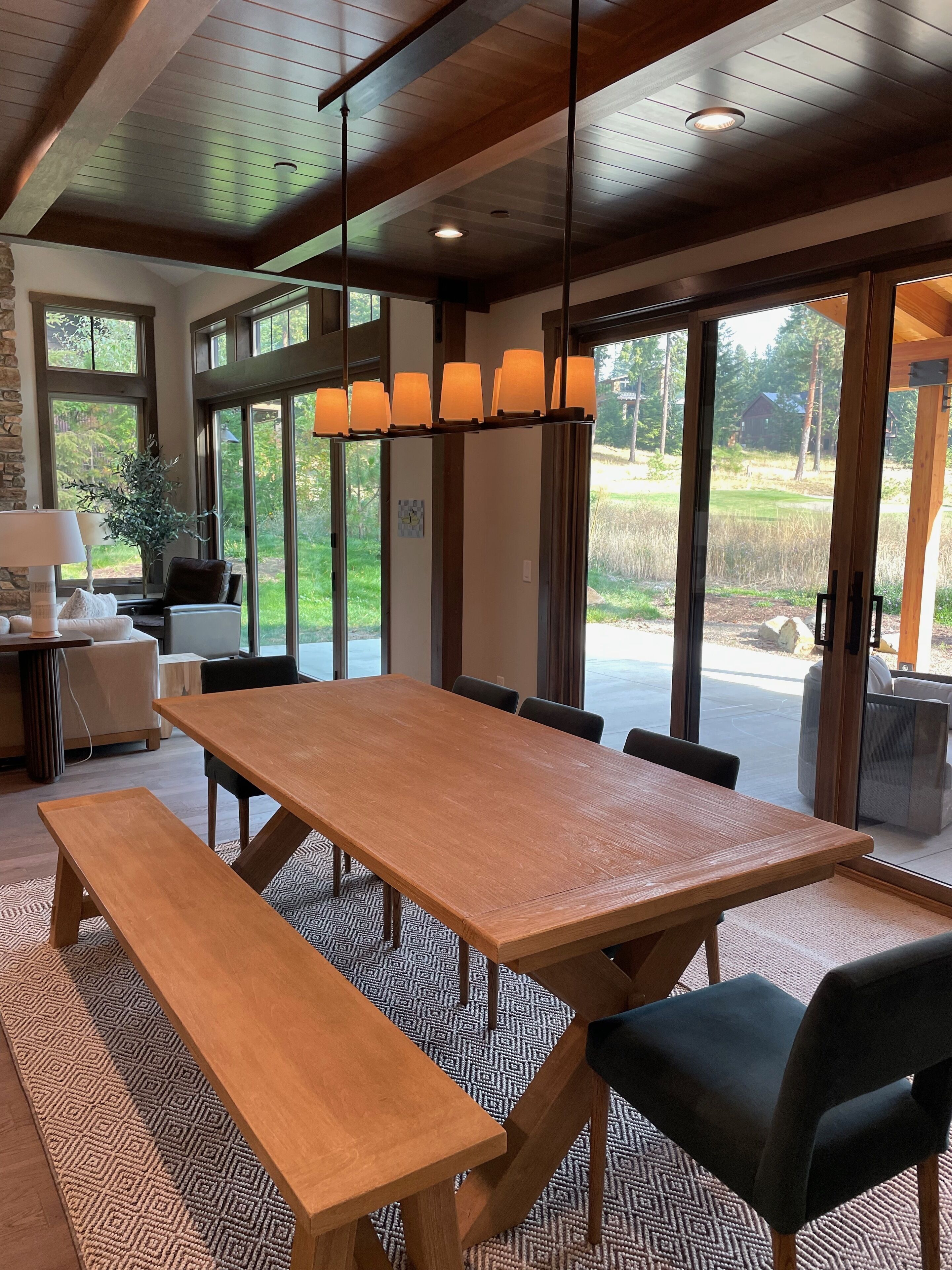 Un comedor amplio con una gran mesa de madera, varias sillas y un banco. Hay ventanas grandes que ofrecen vistas al exterior.