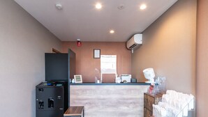 Zona de recepción con mostrador, máquina de café, una mesita y refrigerador.