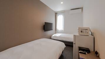Een hotelkamer met twee eenpersoonsbedden, een flatscreen televisie aan de muur, een magnetron op een tafeltje en een raam met gordijnen.