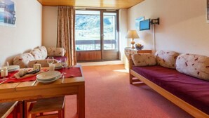 A cozy room with a wooden ceiling, a sofa, a dining table with plates and glasses, and a window with a view of the outdoors. - Les Tommeuses (Val Claret) by Interhome (Tignes)