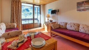 A cozy room with a wooden ceiling, a sofa set, a dining table with plates and glasses, and a window with curtains. - Les Tommeuses (Val Claret) by Interhome (Tignes)