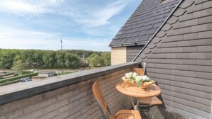 A rooftop terrace with a wooden table and chairs, a flower vase, and a view of a green landscape and trees. - Goldsands II 302 with parking by Interhome (De Haan)